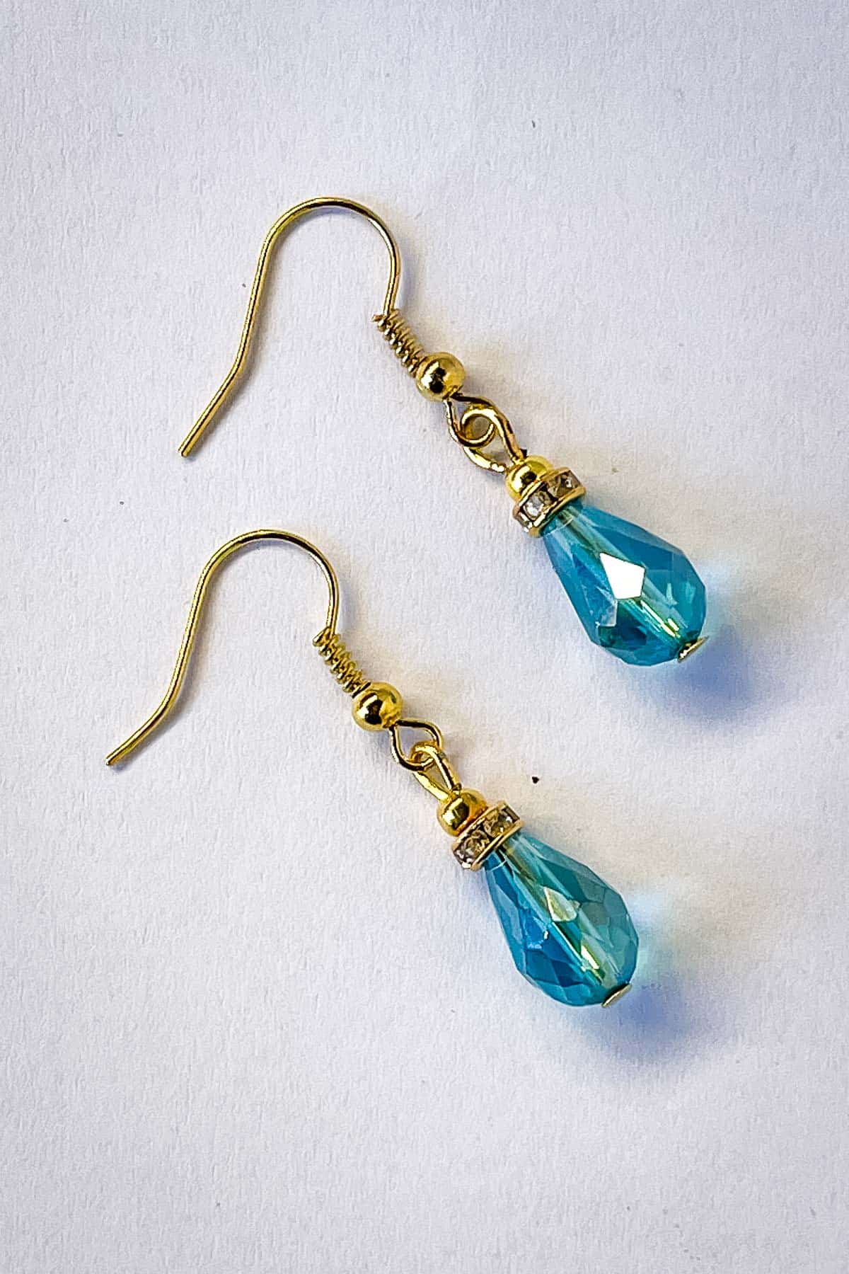 A pair of blue crystal teardrop beaded earrings in gold.