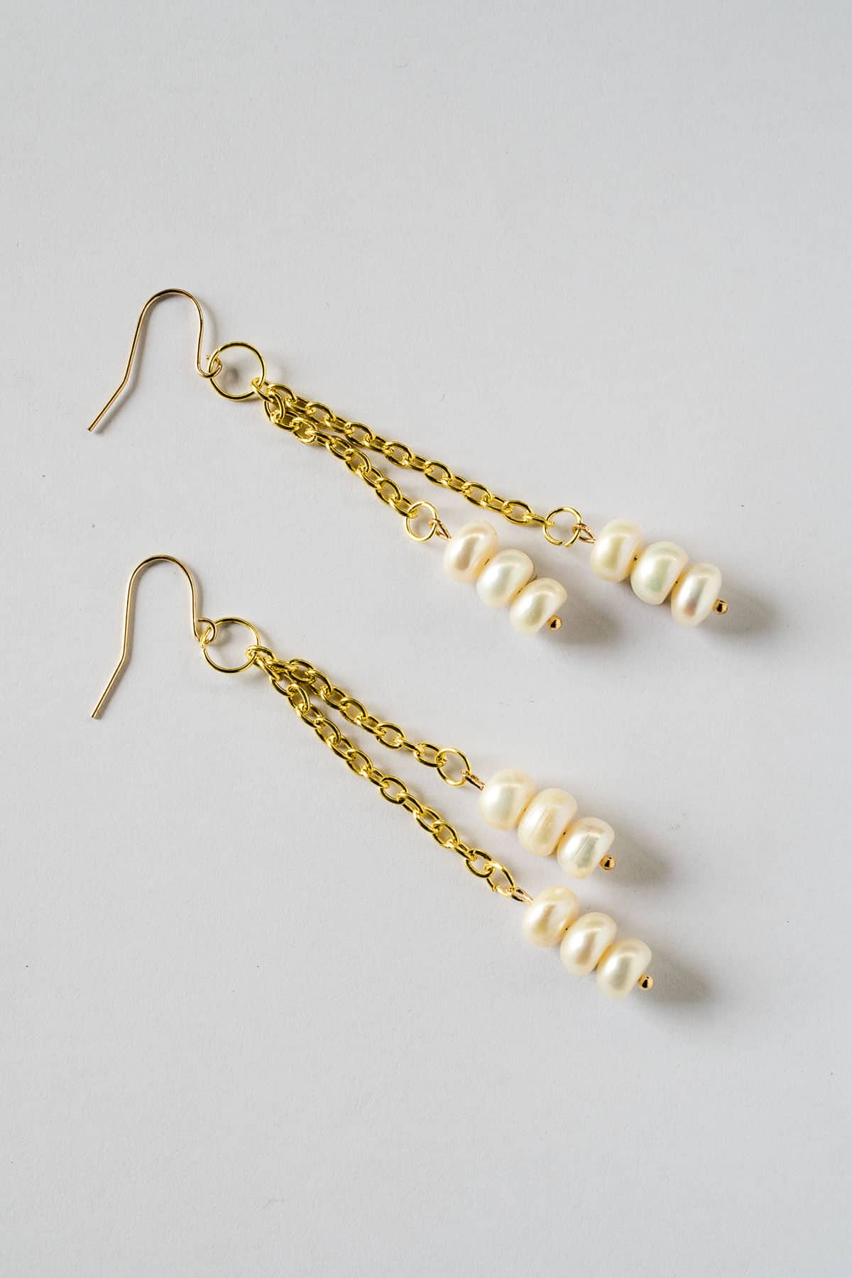 A pair of long white and gold freshwater pearl DIY dangle earrings.