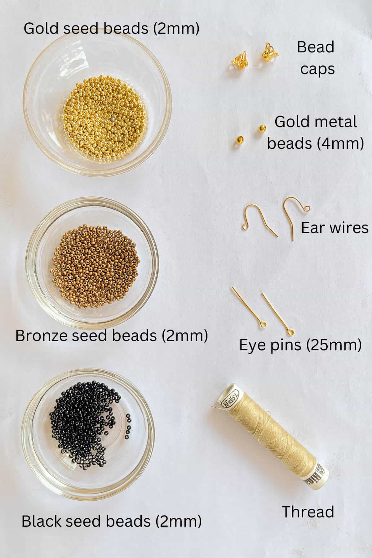 Gold, bronze and black seed beads, bead caps, gold beads, ear wires, eye pins and thread against marble background.