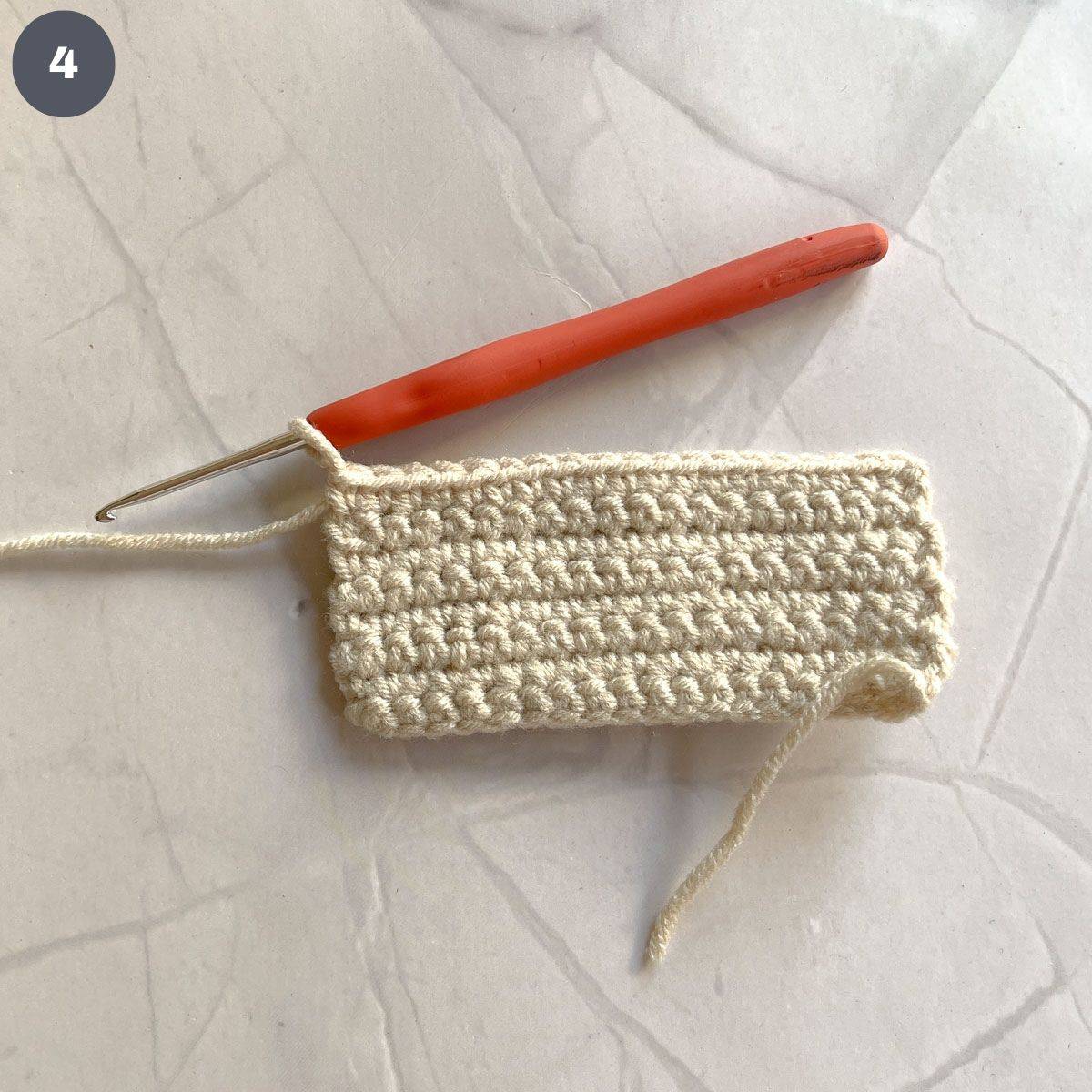 A rectangle crochet piece with hook attached to it.