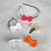 Black hair band with red crochet bow, black snap clip with green crochet bow, brown hair tie with white crochet bow and 2 hair barrettes with white and orange crochet bows each.
