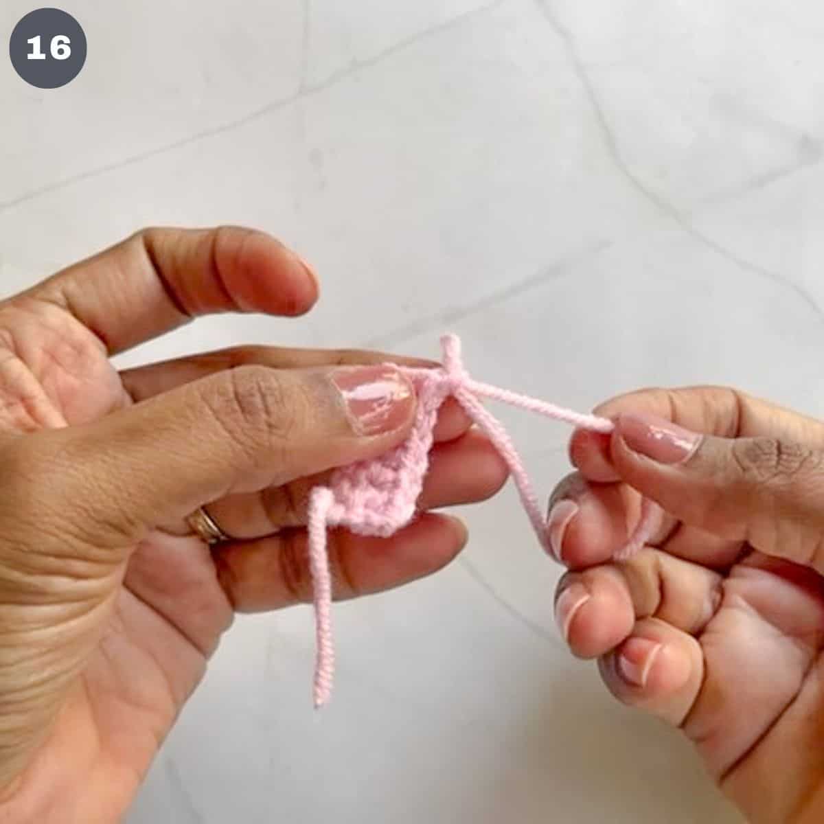 Pulling a pink crochet yarn to fasten stiches.