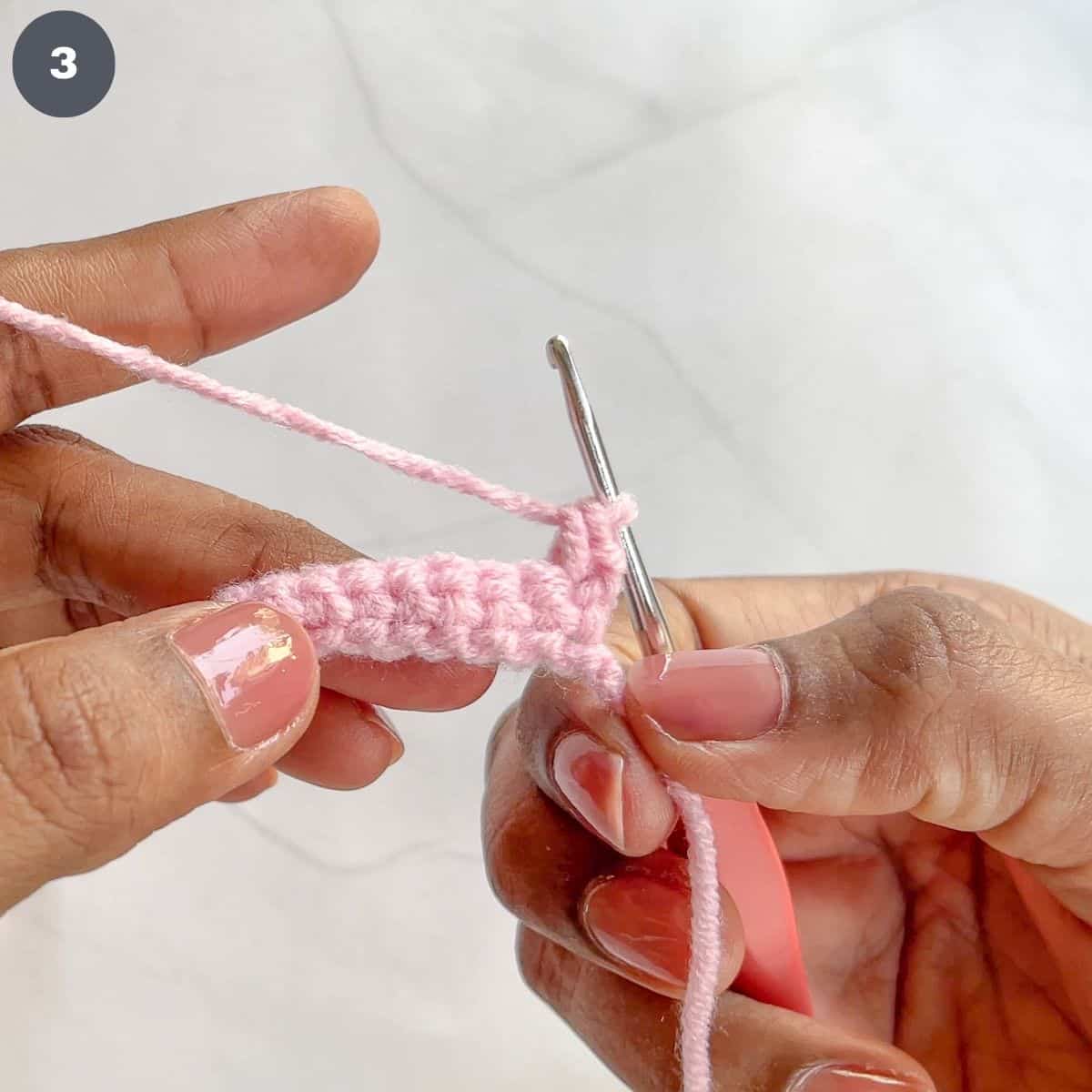 Stitching single crochets with pink yarn.