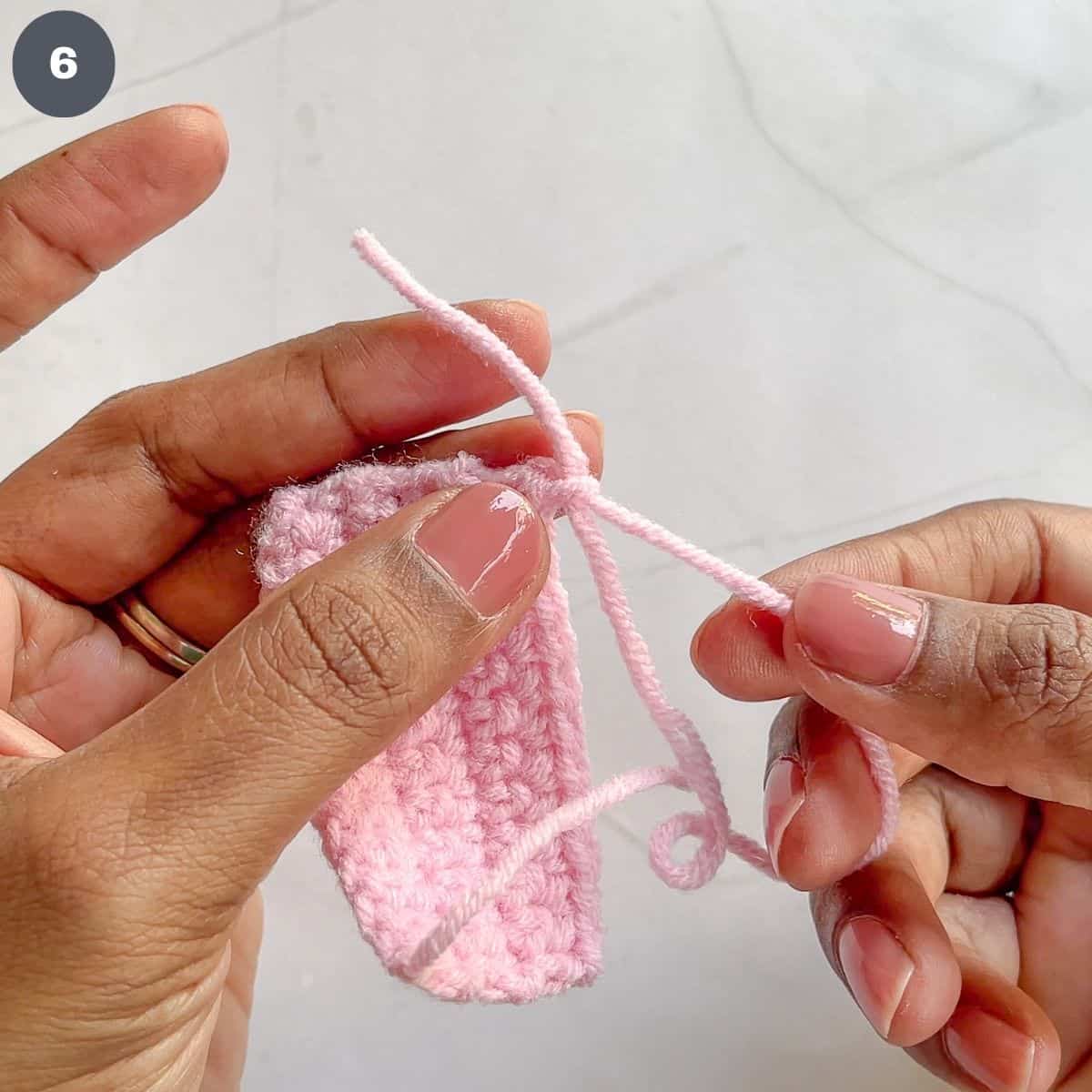 Pulling a pink crochet yarn to fasten stiches.