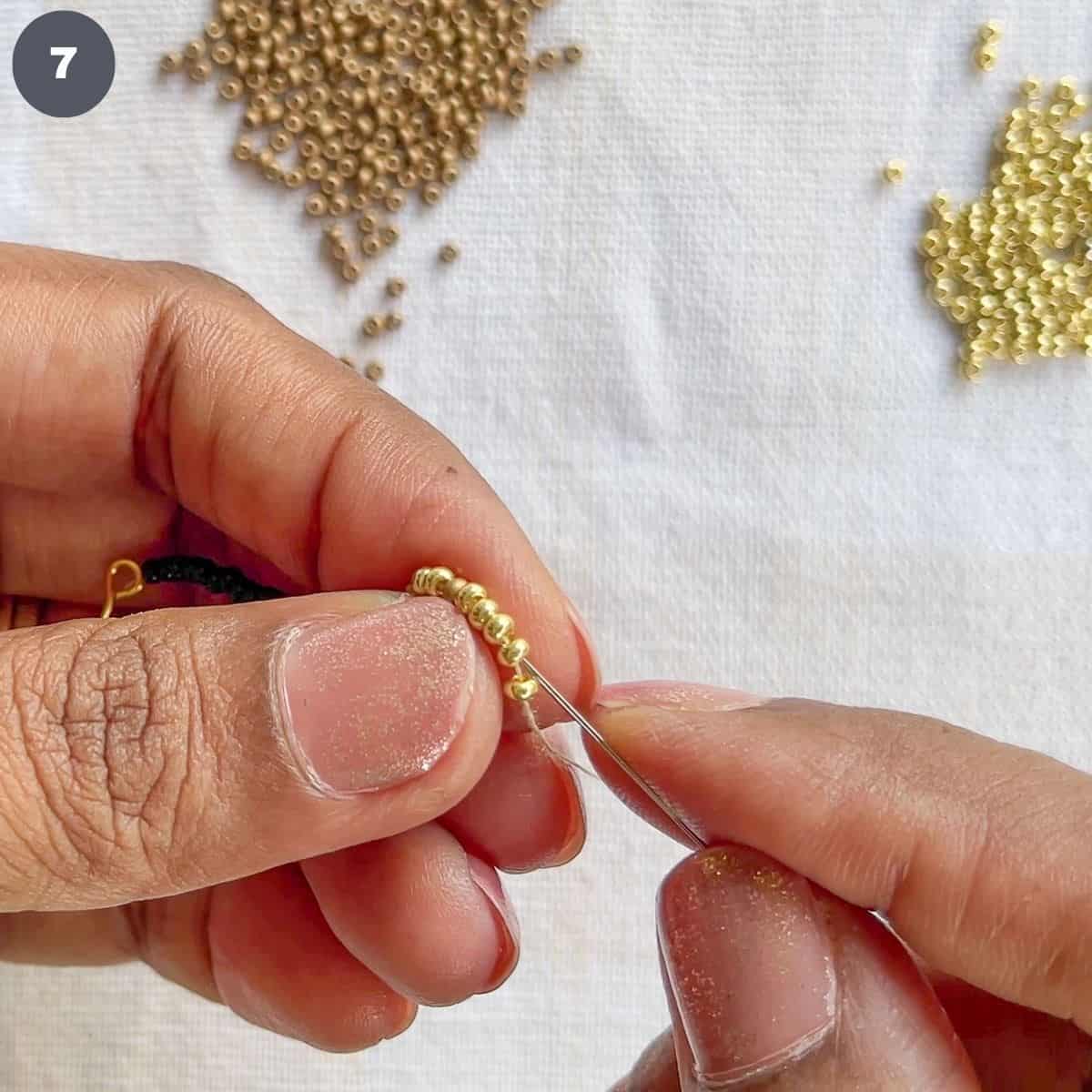Inserting needle into a strand of gold beads.