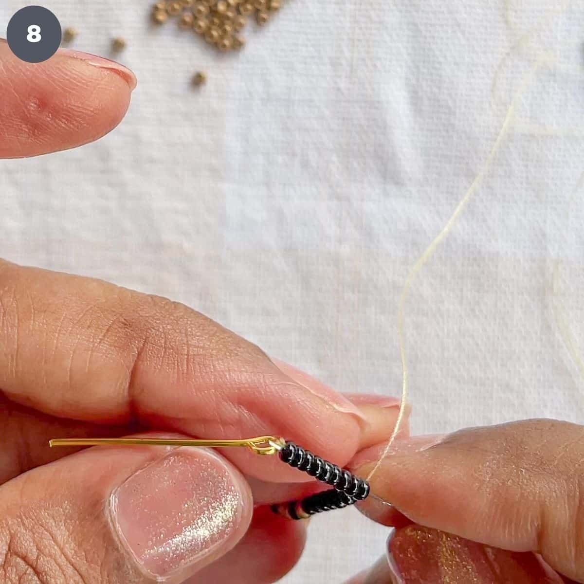 Threading through a strand of black beads with a needle.