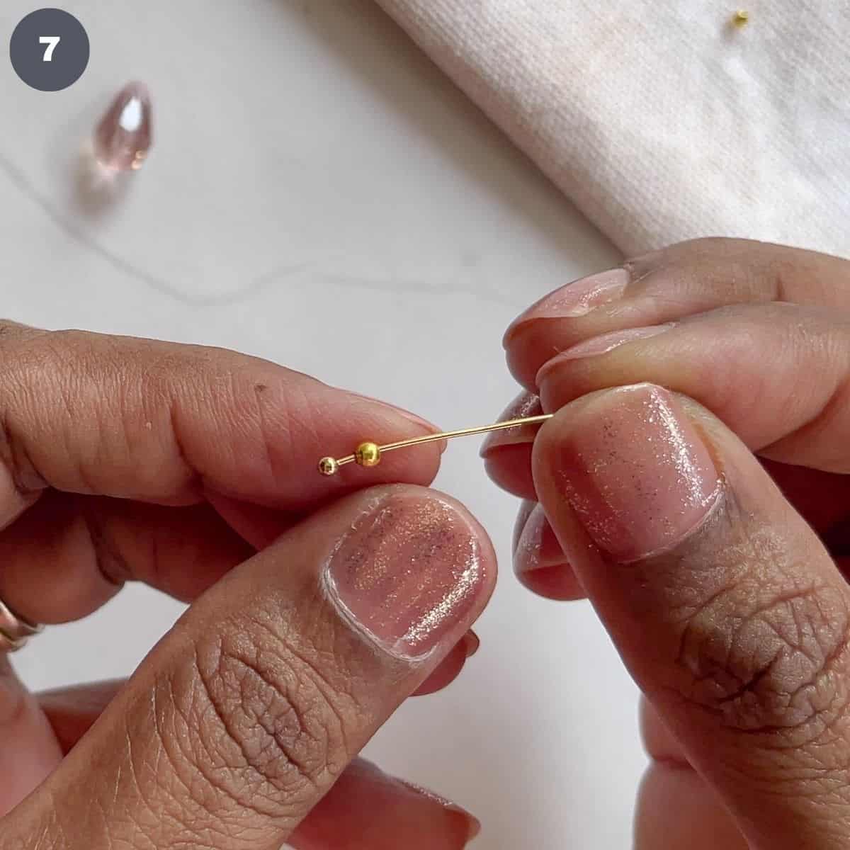 Inserting a gold bead into a head pin.