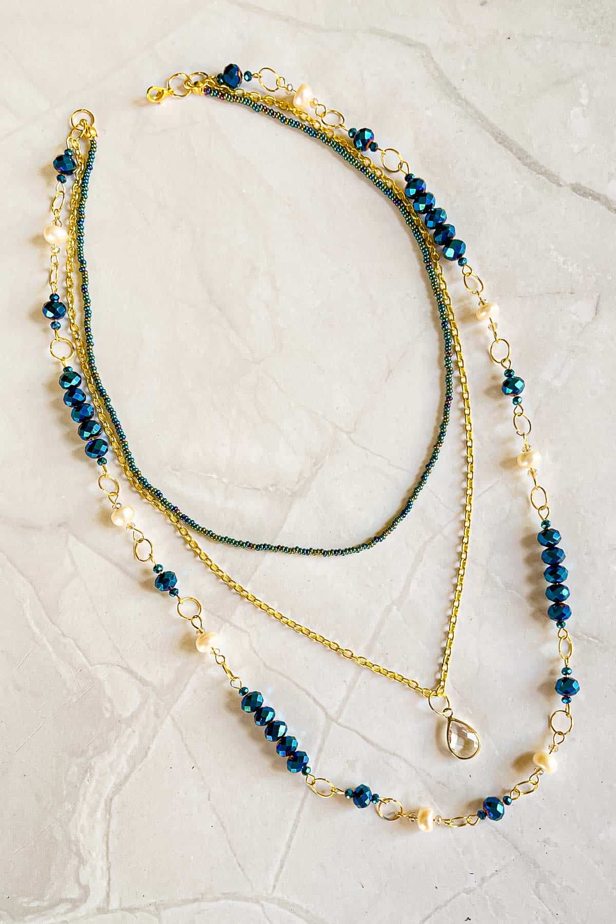 A multi strand necklace with a layer of seed beads, link chain with teardrop pendant and blue and white bead link chain.