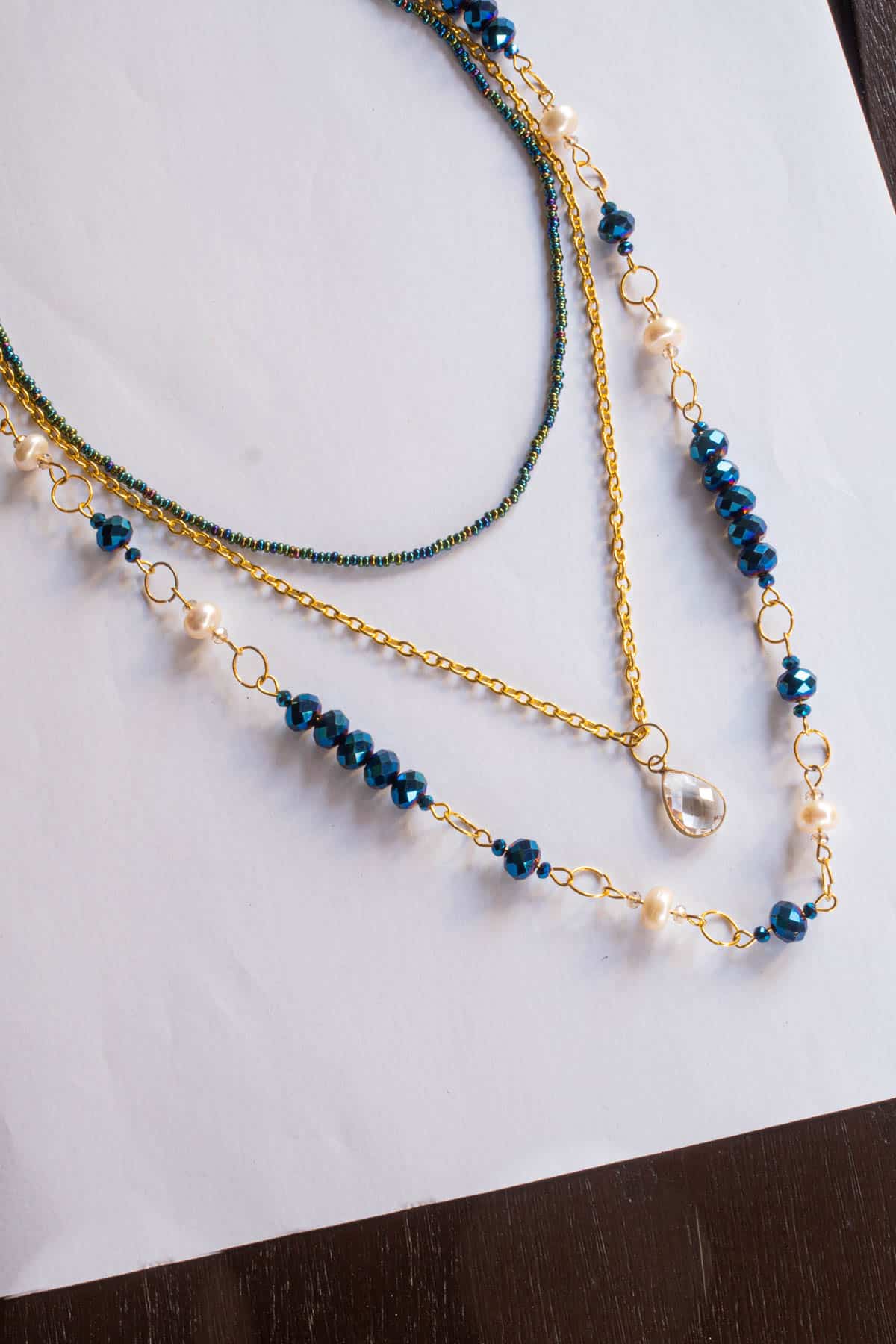 Seed bead strand, gold link chain with a pendant and a blue beads and pearls link chain in layers.
