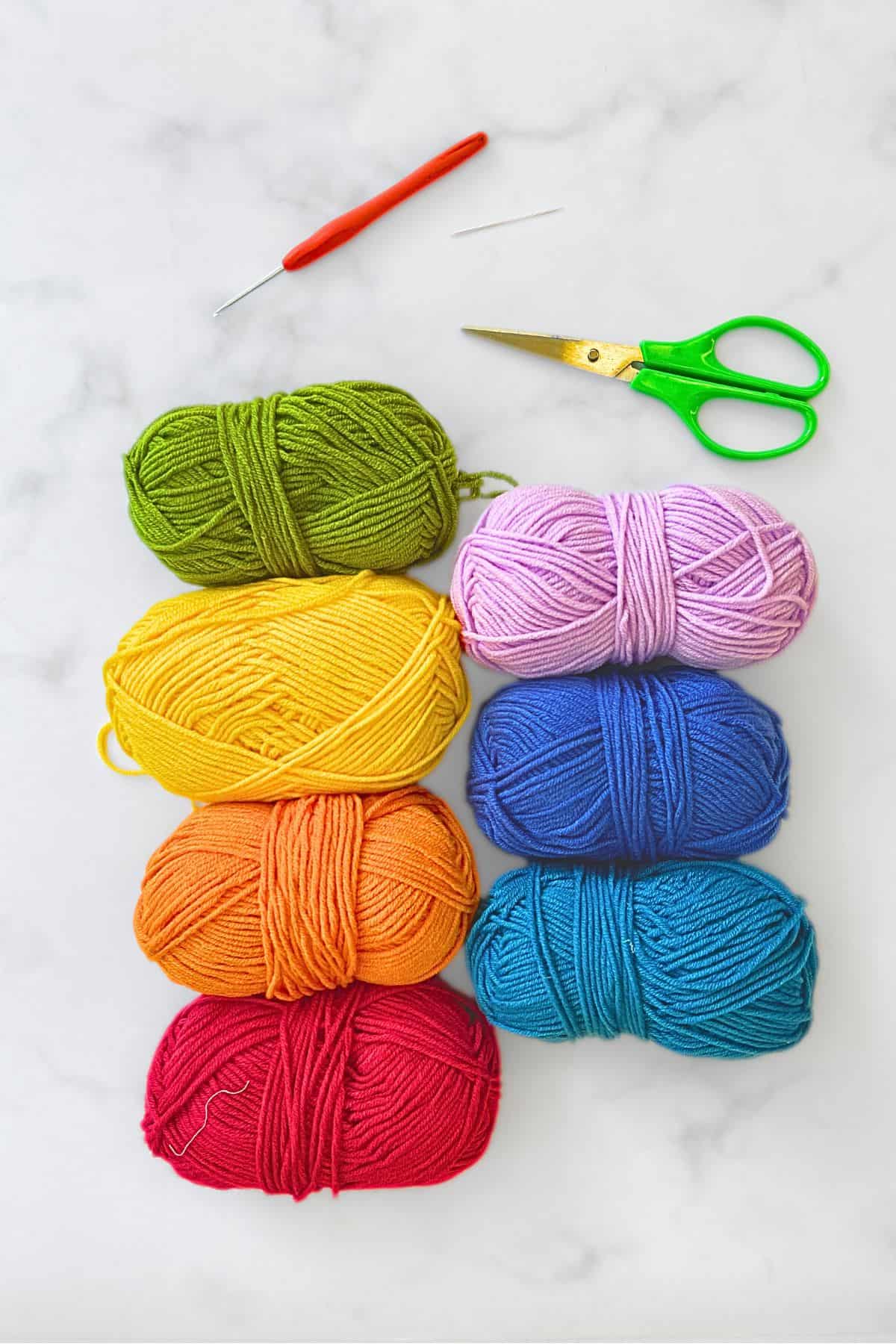 Crochet yarn in 7 rainbow colors, a pair of scissors, a crochet hook and a needle.